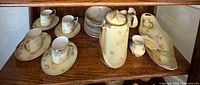 Full lot on shelf showing chocolate pot, four cup-saucer sets, stacked dessert plates, platter, creamer, sugar bowl