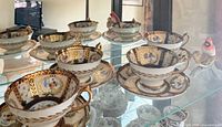Multiple teacups, saucers and cardinal figurine displayed in glass cabinet