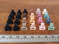 Front view of 24 square matte plastic hair claw clips arranged by color next to ruler