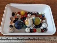 Tray showing full assortment of glass marbles with ruler for scale
