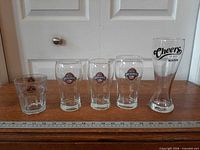 Five assorted branded bar glasses lined beside ruler