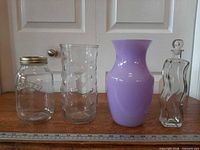 Front view of four glass items lined up: Kilner jar, bubble glass vase, lavender vase, clear decanter with ruler for scale