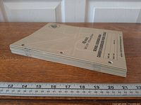 Stack of eight taupe North American Paper exercise books showing spine, three binder holes and ruler for scale