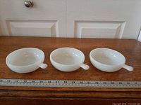Three white milk glass handled soup bowls side by side with ruler