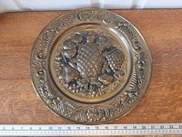 Front view showing entire repoussé brass plate and ruler for scale