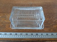 overall view of clear glass butter dish showing embossed "BUTTER" lid and ribbed design with ruler for scale