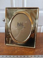 Front view of polished brass rectangular frame with oval opening and insert indicating 8" × 10" size