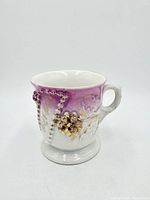Front view of porcelain scuttle mug showing purple gradient, floral relief, beaded garland and handle