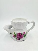 Front view of white porcelain scuttle mug with rose pattern, handle and spout visible