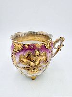 Front view showing pink-purple glaze, raised gilt decoration and feet