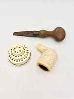 Overall view of meerschaum pipe bowl, wooden-handled metal tool and perforated disc