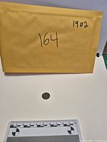 Envelope with lot number and full view of coin for scale