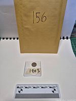 Envelope, coin in plastic sleeve, scale for size reference