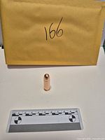 Copper bullet standing upright before scale and envelope