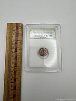 Front view of slabbed coin beside ruler for scale