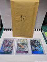 Front view of all three One Piece cards in toploaders with envelope behind