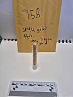 Tube standing upright with envelope marked '24K gold foil very little gold' and scale