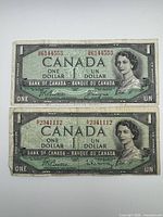 Front of both 1954 $1 notes showing Queen Elizabeth II, serial numbers, signatures and wear