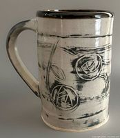 Left side view of tall stoneware mug showing handle and floral design