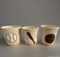 Front view of three signed stoneware cups showing baseball, bat and basketball motifs