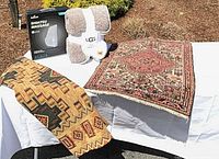 Group shot of throw, boxed massage cushion, two rugs displayed on table outdoors