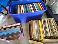 Blue plastic bin filled with boxed set LPs; adjacent cardboard boxes with additional vinyl records