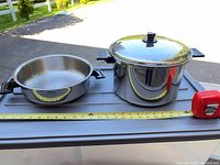 Stock pot with lid and sauté pan side by side with tape measure