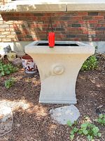 Front view of beige square pedestal planter in garden setting