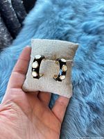 Front view of black enamel huggie hoops with white dots on display pillow