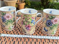 Front view of three matching floral butterfly mugs with ruler for scale