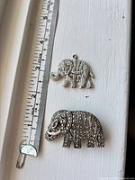 Front view of both elephant jewelry pieces beside ruler