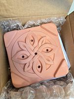Terracotta flower-press slab inside original cardboard box, showing decorative motif and bubble wrap