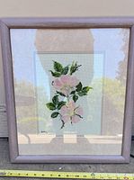 Full view of framed cross-stitch with measuring tape for scale