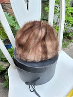 Brown mink fur pillbox hat resting on round hat box, top view of fur texture