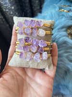 Five gold-tone cuff bracelets with purple amethyst stones displayed on linen pillow
