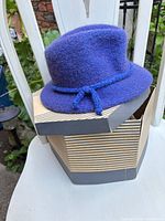 Side view of purple-blue cloche hat resting on striped Fairweather hat box