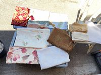 Overview of all folded linens on two tables: six cloths/runners plus napkin stack