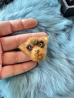 Front view of fur brooch showing face details, held in hand for scale