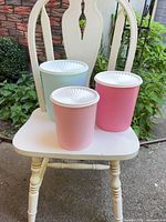 Three plastic canisters in blue, pastel pink and bright pink on chair