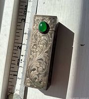 Front view showing floral engraving, green cabochon, ruler for scale