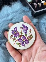 Front view showing floral enamel design and scale in hand