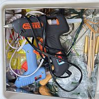 Top view of black and blue corded hot glue guns with glue sticks and other craft items