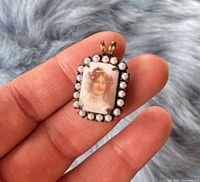 Front view of pendant showing portrait plaque and seed pearl border held in hand for scale