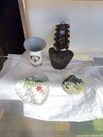 Group shot of porcelain vase, cowbell with strap, heart-shaped dish, and miniature house figurine