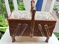 Full view of wooden cantilever sewing box closed, showing legs, arms, handle, floral padded top