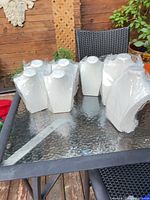 Seven white necklace display busts on glass table, most in plastic wrap