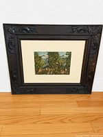 Full view of framed print leaning against wall showing carved wood frame and mat