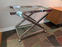 Full view of chrome and glass bar cart against wall