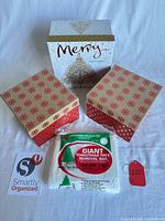 All items grouped: large white Merry box, two red/gold boxes, packaged tree bag, canvas pouch