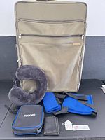 Suitcase standing with neck pillow, blue straps, Escort pouch, wallet and tags displayed